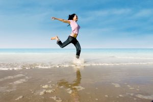 happy woman running through waves at the beach